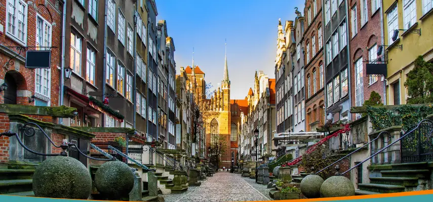 Mariacka Street in Gdańsk with stone gargoyle waterspouts, colorful merchant houses, and St. Mary's Basilica tower in the background