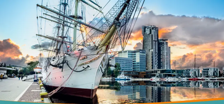 Dar Pomorza tall ship moored at the Gdynia waterfront with the Sea Towers skyscrapers in the background at sunset
